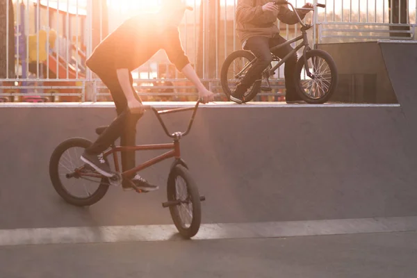 Two bmx cyclists riding a bike on a park skate on the background of the sunset. Bmx Concept. — Stock Photo, Image