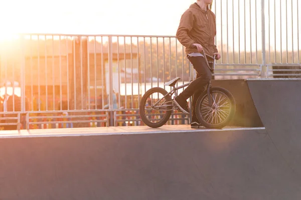 BMX cyclist is standing on a ramp skate park on the background of the sunset. Bmx bicycle and cyclist on the sunset. Copyspace. — Stock Photo, Image