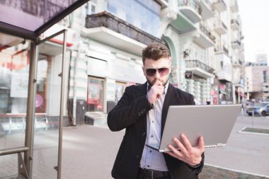 Bir iş adamı ayakta dışında ve bir laptop arıyorum. Açık havada bilgisayarda çalışır. İşe giderken çalışır çünkü adam zaman, yok.