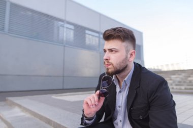 Düşünceli bir işadamı, modern mimarinin arka sokakta oturuyor. Düşünen bir iş adamı portresi. İş kavramı. Beyin fırtınası.