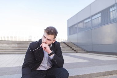 Hayal kırıklığına uğramış işadamı hüzünlü, merdiven üzerinde oturuyor. Bir depresif adam sokakta oturuyor. Üzücü bir işadamı portresi. İş kavramı.