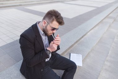 Sokakta oturan ve bir sigara yakışıklı iş adamı. Merdivenlerde oturan ve bir sigara depresif iş adamı