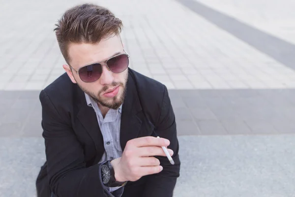 Retrato de perto de um homem de negócios de óculos e um cigarro nas mãos. Bom empresário fumar um cigarro ao ar livre — Fotografia de Stock