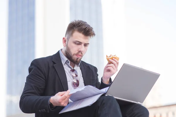 Портрет зайнятого чоловіка з ноутбуком, бізнес-паперами та закусками під відкритим небом. На вулиці працює зайнятий бізнесмен — стокове фото