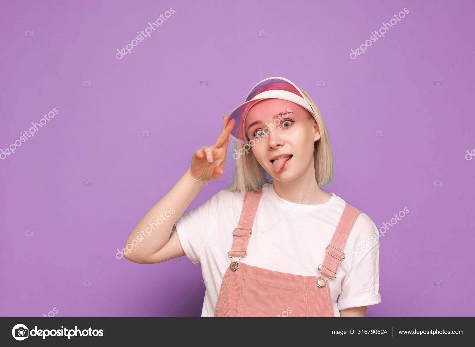 ピンクの帽子をかぶって紫色の背景に面白い顔をして かなりカジュアルなドレスで面白い女の子の肖像画 面白いですティーン女の子posesオンカメラ 隔離されたクローズアップポートレート ストック写真 C Bodnarphoto