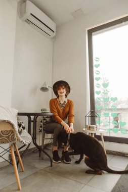 Mutlu kız rahat bir kafede bir fincan kahveyle masaya oturur, tasmalı bir köpeği tutar, kameraya bakar ve gülümser. Gülümseyen bayan hippi köpeğiyle kafeye girer ve kahve içer.