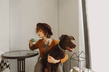 Çekici kız güzel kahverengi bir köpeği kucaklıyor ve içine kahve içiyor. 