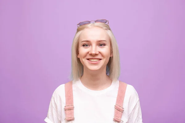 Στενή προσωπογραφία ενός χαμογελαστού έφηβου κοριτσιού σε μωβ φόντο, φορώντας ένα t-shirt, κοιτάζοντας στην κάμερα και πανηγυρίζοντας. Θετικό κορίτσι απομονωμένο σε ροζ φόντο. — Φωτογραφία Αρχείου