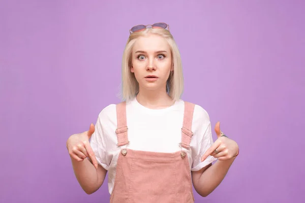 Sorpresa ragazza bionda in abiti carini si erge su un backgrou viola — Foto Stock