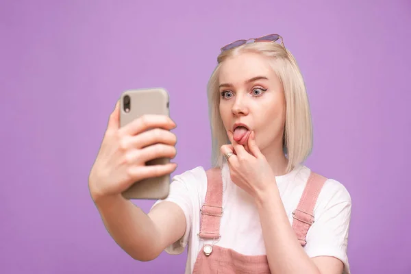 Menina engraçada com cabelo claro fazendo uma selfie em um fundo roxo — Fotografia de Stock