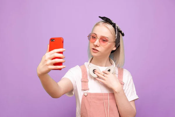 Menina elegante em fones de ouvido e roupas brilhantes faz uma selfie em — Fotografia de Stock