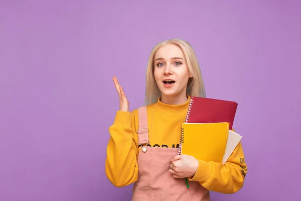 Joyeux étudiant fille en vêtements décontractés debout sur un fond violet avec des livres et des cahiers dans ses mains, regardant dans la caméra.Portrait d'un étudiant, tenant un cahier dans ses mains.Concept d'apprentissage — Photo