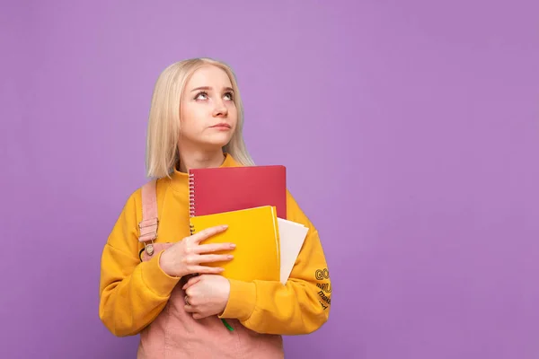 Στοχαστικό κορίτσι μαθήτρια με σημειωματάρια στα χέρια του κοιτάζει πέρα σε ένα κενό χώρο, απομονωμένο σε ένα πορφυρό φόντο. Πορτραίτο ενός εφήβου σε ροζ φόντο. Εκπαιδευτική έννοια. — Φωτογραφία Αρχείου