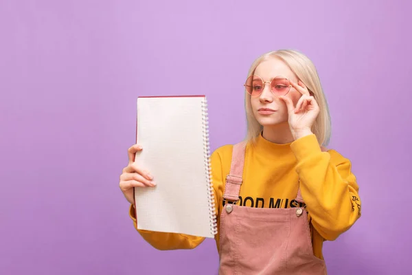 Εστιασμένη ελκυστικό κορίτσι με φωτεινά ρούχα και ροζ γυαλιά ηλίου διαβάζει ένα σημειωματάριο με μια συγκεντρωμένη έκφραση προσώπου. Πορτρέτο ενός αστείος Έφηβος με ένα σημειωματάριο στο χέρι του. Απομονωμένες. — Φωτογραφία Αρχείου