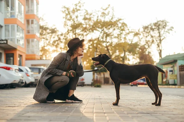 Belle fille dans des vêtements élégants et chapeau jouer avec le chien sur st — Photo