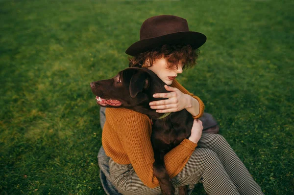 Nahaufnahme Porträt eines Mädchens, das auf einem grünen Rasen sitzt und einen schönen braunen Hund umarmt, Draufsicht. attraktive Dame umarmt den Welpen fest. Liebe zu Haustieren. — Stockfoto