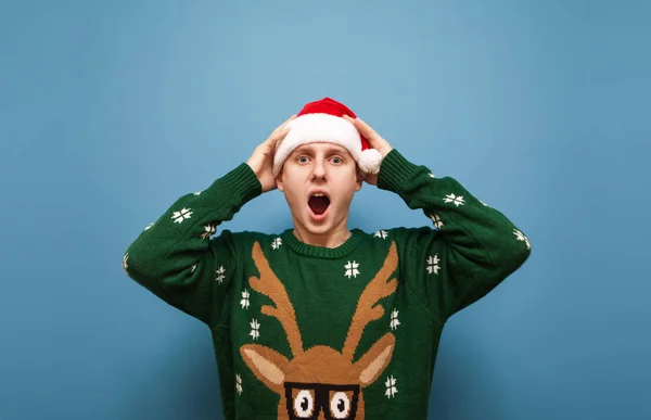 Ritratto di ragazzo scioccato in cappello di Babbo Natale e maglione verde caldo, sorpreso dalla sorpresa, guardando nella fotocamera con la bocca aperta. Isolato. Oh mio Dio. WoW — Foto Stock