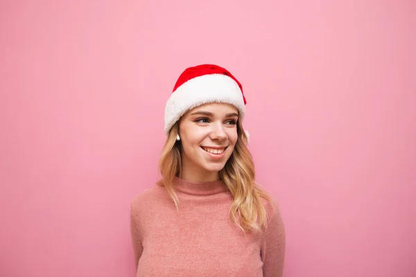 Ritratto di una ragazza carina con maglione rosa e cappello di Natale, che ascolta musica con cuffie senza fili, distoglie lo sguardo da uno spazio vuoto e sorride. — Foto Stock