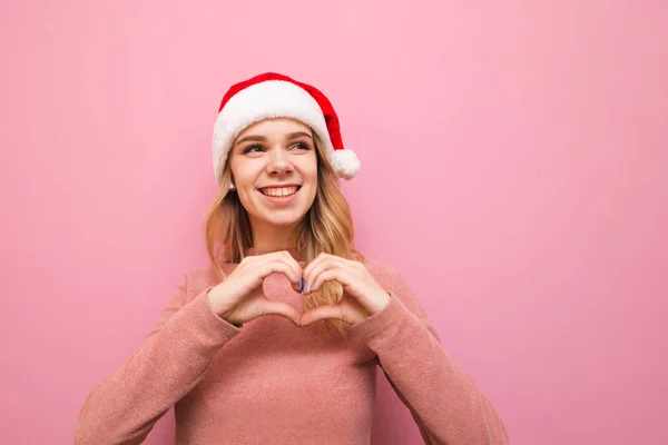 Söt leende flicka i en hatt av jultomten står på en rosa baksida — Stockfoto