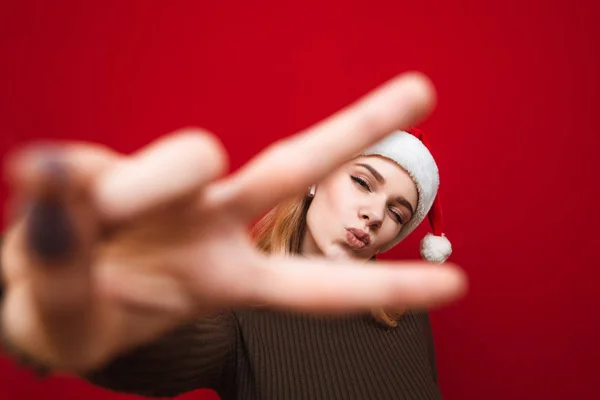 Retrato de chica feliz en suéter caliente se levanta sobre fondo de pared roja, muestra gesto de la mano de la paz, mira a la cámara y muestra un kiss.Joyful dama en suéter posa para la cámara aislada en rojo —  Fotos de Stock