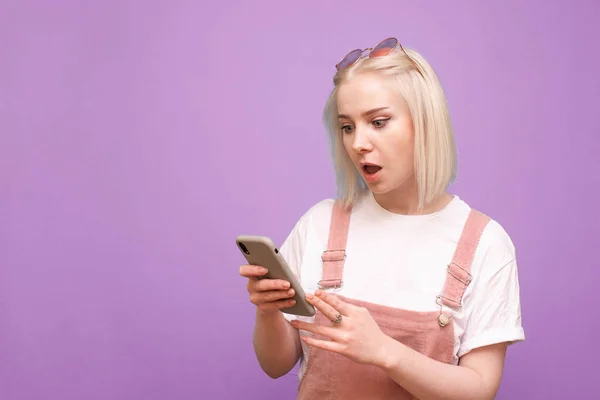 Surpreendida adolescente com cabelo claro, usa um smartphone em um p — Fotografia de Stock