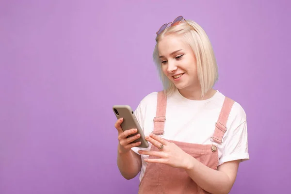 Menina sorridente adolescente com cabelo claro, usa um telefone em um roxo — Fotografia de Stock