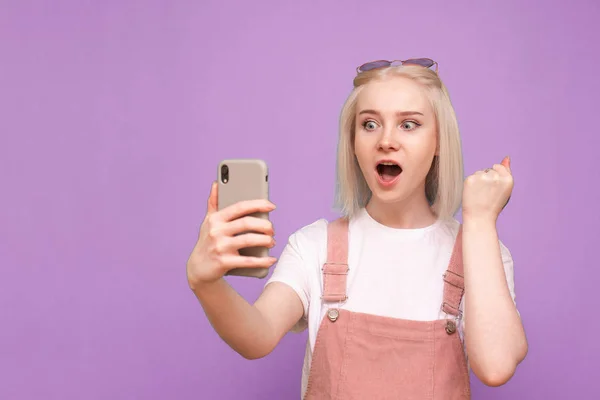 Menina loira alegre em uma roupa casual brilhante detém um smartphone — Fotografia de Stock