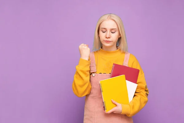 Attrayant étudiant fille aux cheveux clairs se tient avec des livres et des cahiers dans ses mains et est en colère avec un fond violet. Portrait d'un étudiant insatisfait de ses études, isolé . — Photo