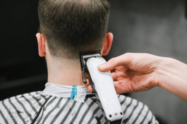 Barber's hand with a clipper cuts the back of a man's neck. Haircuts in barbershop. Hairdresser shaves a young man hair clipper. Men's haircuts in the man beauty salon. Background. Copy space