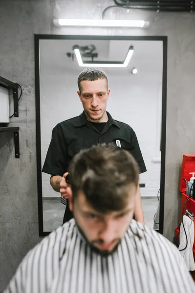 Вертикальний портрет перукаря вирізає бородатого клієнта в чоловічому перукарні, дивлячись уважно на чоловіче волосся. Чоловічий перукар створює зачіску. Концепція перукарні — стокове фото