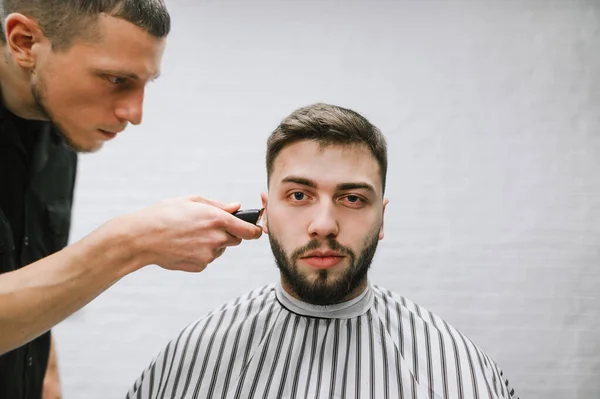 L'homme à la barbe visite un salon de coiffure, un coiffeur répète en créant une coiffure avec une tondeuse à la main. Coiffeur professionnel fait coiffure élégante pour un beau client dans un coiffeur masculin — Photo