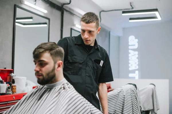 Portrait of a barber with a clipper in his hand and a bearded man sitting in a chair, a hairdresser makes a stylish men's haircut in a barber shop. Concentrated male hairdresser hair cut bearded man — Stockfoto