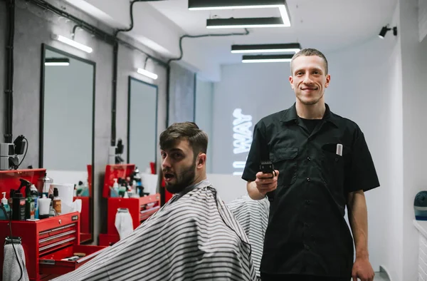 Porträt eines glücklichen Friseurs, der mit Klipper in der Hand in der Nähe von Cha steht — Stockfoto