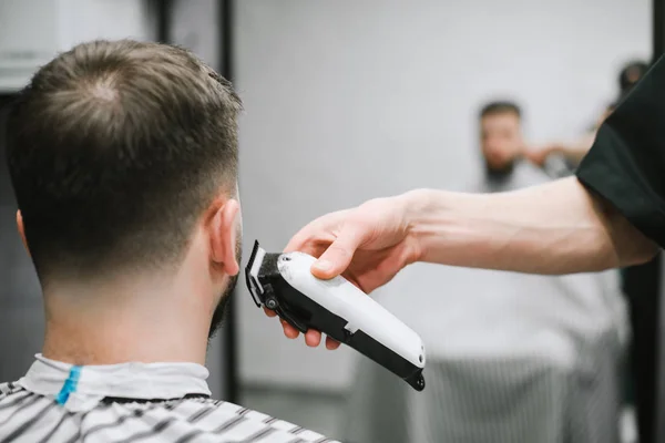 Die Hand eines Friseurs mit einem Haarschneider schneidet einem Mann den Nacken auf. Friseursalon. Friseur rasiert einem jungen Mann den Haarschneider. Männerfrisuren im Männer-Schönheitssalon. Hintergrund. Kopierraum — Stockfoto