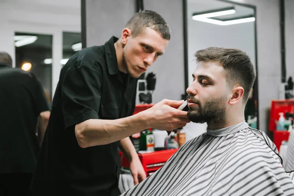 Професійний перукар з кліпкою в руці робить зачіску для клієнта. Людина отримує службу в перукарні, перукаря займається виправленням бороди.. — стокове фото