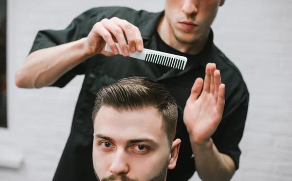 Closeup photo of a barber styling a man's hair. Hairdresser completes the haircut of the client. Hair styling with wax and comb on model's head. Barbershop concept. — Stockfoto