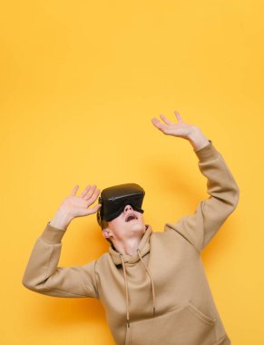 Joyful young man in VR helmet stands on yellow background, looks up with surprised face and mouth open. porter of surprised guy in virtual reality helmet looking at copy space. Vertical