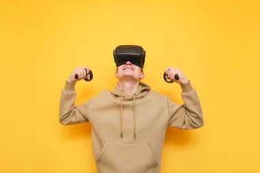 Portrait of joyful young gamer man in VR glasses and controllers