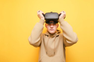 Young man in a virtual reality helmet and with controllers in his hands playing VR games, looking at the camera, copy space. teenager in VR helmet isolated.