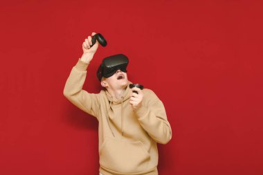 Portrait of emotional young man playing VR games with controller in hands and virtual reality helmet, looking up with surprised face. Funny guy gamer playing games in VR helmet.