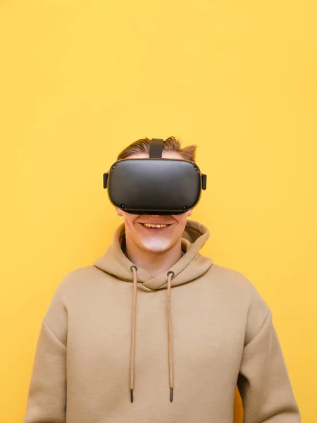 Portrait de jeune homme heureux en casque vr sur fond jaune, regardant dans la caméra et souriant. Il joue à des jeux VR. Adolescent joyeux avec casque VR isolé sur fond jaune. vertical — Photo