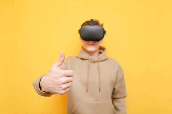Le gars heureux en réalité virtuelle casque et vêtements décontractés se tient sur un fond jaune et montre pouces vers le haut gros plan. Jeune homme aimerait utiliser la technologie VR qu'il recommande.Copier l'espace. Contexte . — Photo