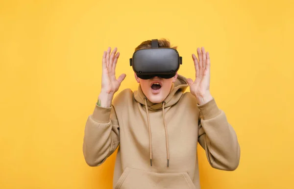 Portrait de jeune homme choqué en réalité virtuelle casque sur fond jaune, leva les mains vers le haut dans l'étonnement. Guy dans le casque VR joue à des jeux vidéo à la surprise de regarder la caméra . — Photo