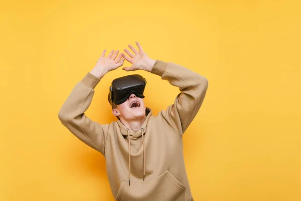 Portrait de jeune homme émotionnel dans des lunettes VR sur fond jaune, levant les mains et levant les yeux de la bouche couverte. Joueur expressif utilise un casque VR. Isolé . — Photo