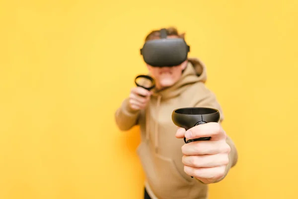 Main avec contrôleur, photo rapprochée sur fond de jeune homme dans le casque VR. Guy en vêtements décontractés joue à des jeux vidéo de réalité virtuelle à l'aide d'un casque VR. L'homme boxe en VR. Contexte. Espace de copie — Photo