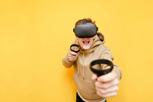 Happy guy dans un casque VR joue à des jeux en réalité virtuelle, regarde à la caméra avec un visage heureux et montre les contrôleurs à la caméra. Joueur émotionnel joue VR avec un casque de réalité et contrôleurs. — Photo