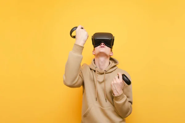 Joueur joyeux dans un casque VR et avec des contrôleurs dans leurs mains est heureux de gagner le jeu vidéo. Jeune homme jouant VR dans un casque, isolé. Concept de réalité virtuelle . — Photo