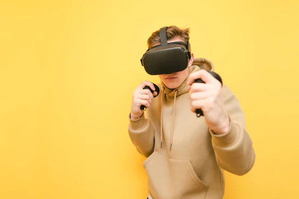 Jeune homme boxant sur un fond jaune avec des contrôleurs dans ses mains et un casque de réalité virtuelle sur la tête. Le gars au casque VR joue à un jeu vidéo, avec un visage sérieux isolé sur un jaune — Photo