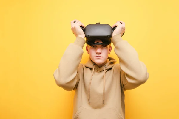 Jeune homme dans un casque de réalité virtuelle et avec des contrôleurs dans ses mains à jouer à des jeux VR, en regardant la caméra, copier l'espace. adolescent dans VR casque isolé . — Photo