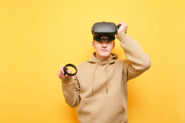 Portrait de type positif dans le casque VR sur la tête isolé sur fond jaune, posant à la caméra. Joyeux jeune joueur masculin jouant à des jeux VR, souriant et regardant la caméra — Photo